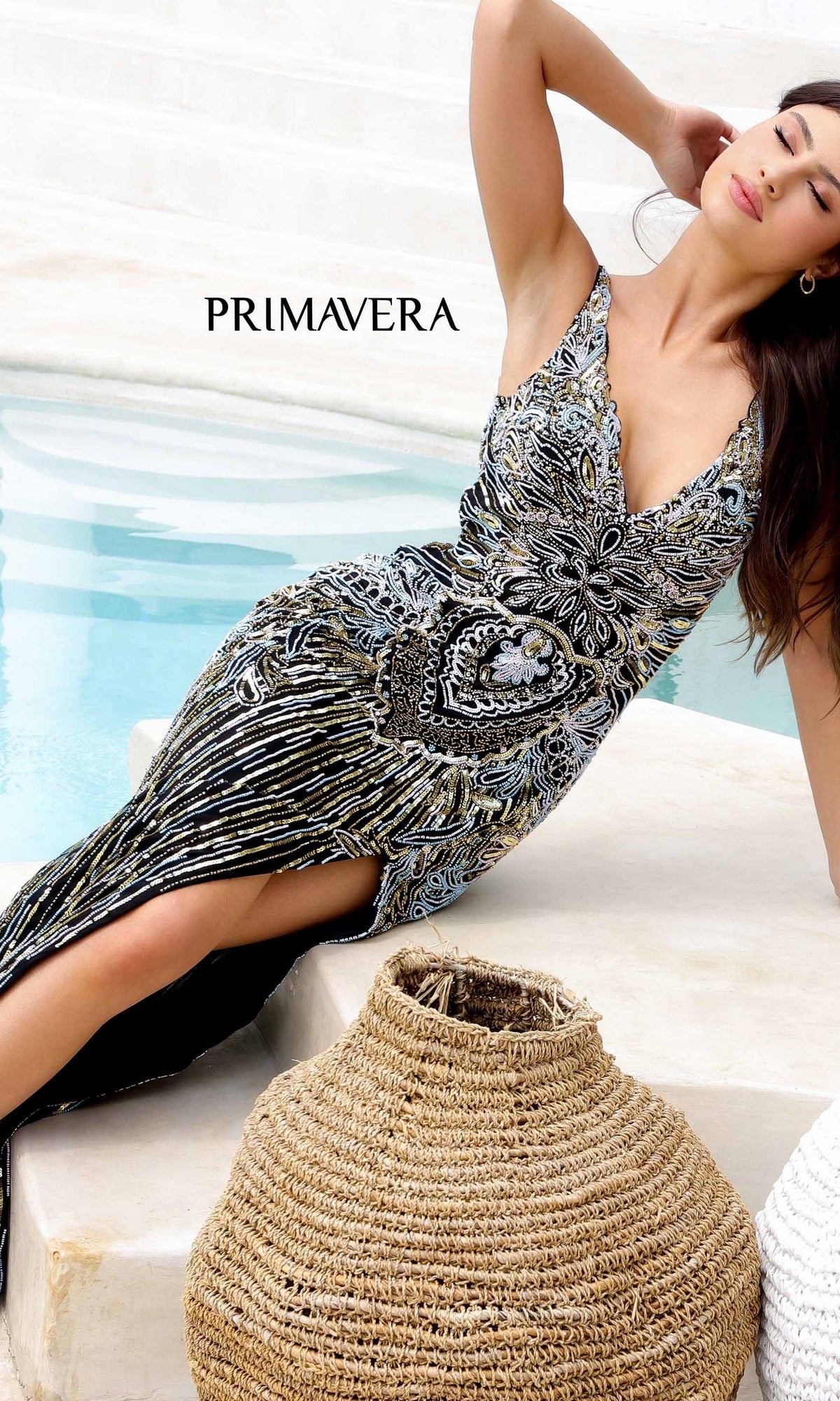 A woman in the Long Formal Dress 4299 by Primavera, featuring a v-neck and beaded details, poses poolside beside woven baskets with